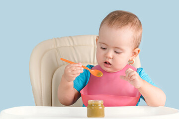toddler aged 12-23 months sits on a feeding chair and learns to eat broccoli puree from a glass jar...