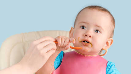 Mom teaches a newborn baby 12-17 months old to use a spoon while eating