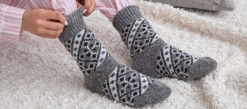 Woman putting on her warm knitted socks at home. Concept of heating season