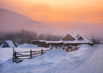 winter village landscape, farm and wooden houses in the countryside, fog at sunset in the mountains.