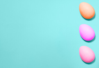 Three Easter eggs colored with violet, pink and coral colors from right side on a blue background. Flat lay. Copy space for text, mock up. Banner.