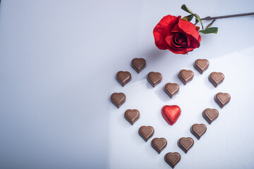 Closeup of heart shaped chocolate confections, and red roses against a bright white background.