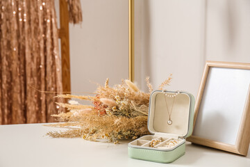 Opened box with stylish jewelry, photo frame and flowers on white table