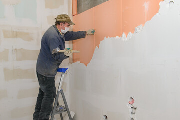 A worker on a stepladder breaks a wall of plaster blocks
