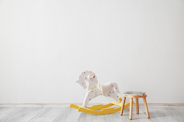 Rocking horse and stool with books near light wall