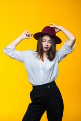 Emotional portrait of a beautiful brunette in a hat and a white shirt on a yellow background
