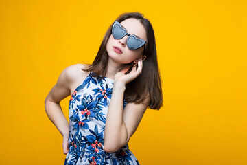 Portrait of a beautiful young woman in a dress and sunglasses on a yellow background