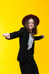 Brunette in a suit and hat dancing on a yellow background