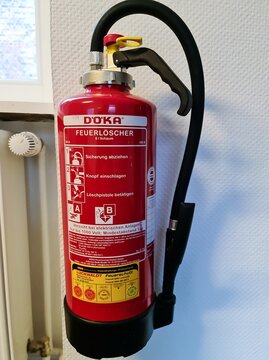 Doka brand red fire extinguisher on white office wall