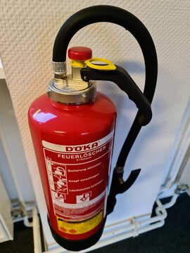 Doka brand red fire extinguisher on white office wall
