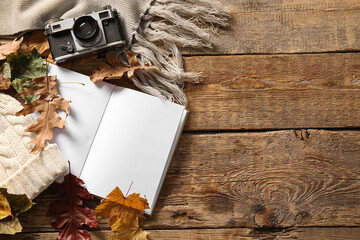 Blank book, warm hat, photo camera and autumn decor on wooden background