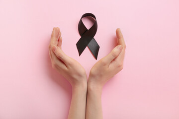 Female hands with black ribbon on pink background. Melanoma concept