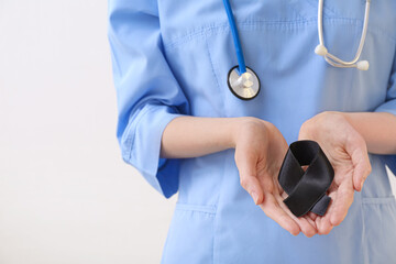 Doctor with black ribbon and stethoscope on light background. Melanoma concept - Powered by Adobe