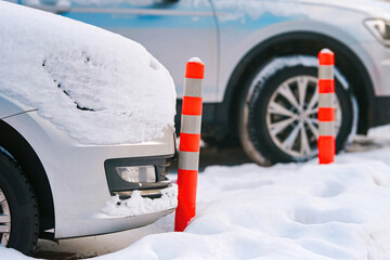 Damaged car bumper and plastic barrier closeup. Car parked close to flexible orange traffic reflective bollard. Plastic parking barrier, prevent car parking on pedestrian area. Winter parking problems