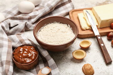 Bowl with flour and ingredients for preparing walnut shaped cookies with boiled condensed milk on light background