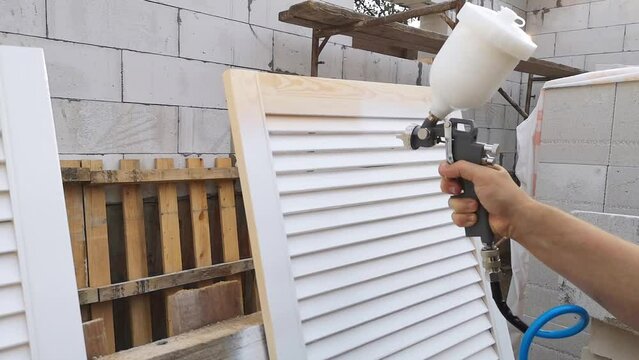 Close-up of a spray gun in a man hand. The process of painting the boards with white paint. Finishing finish. Restoration of old furniture. Compressor operation. Work tool. Fast and easy. Copy space.
