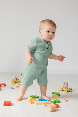 cute baby in a green cotton bodysuit is sitting on the wooden floor of the house playing educational wooden toys. products for children, early development, nursery kindergarten. space for text.