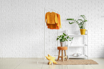 Rack with children's sweaters and shelf unit with houseplants in room interior