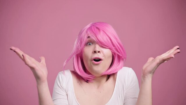 Portrait of shocked woman on pink background. Young female in pink wig has her head boiled.