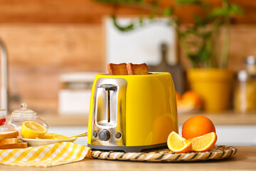 Yellow toaster with bread slices and citrus fruits on table in kitchen