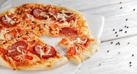 Hot pepperoni pizza on baking paper on white wooden background