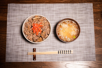 Japanese lunch set of a bowl of popular Japanese food Gyudon served with pickled ginger (beef and onions in a bowl on rice), a bowl of traditional soup Miso and chopsticks