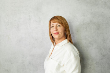 Beautiful middle-aged woman  in a white blouse on a gray background