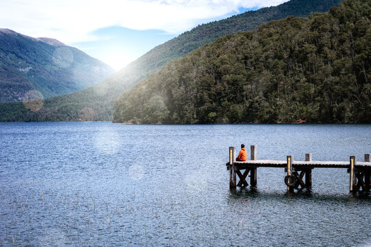 Hombre sentado en soledad en muelle de lago de la patagonia argentina