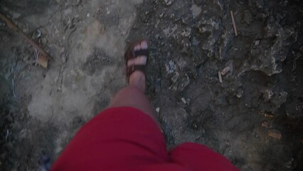 Young male in swimmers walking over rocky path in sandals. Summer vacation POV