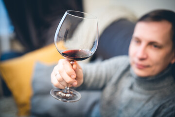 Relaxed serene rich lonely middle aged single man drinking red wine relaxing on sofa at home, enjoying resting sitting on couch holding glass tasting and reflecting.