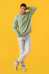 Handsome African-American guy in knitted sweater on yellow background