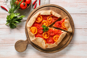 Board with tasty tomato galette on light wooden background