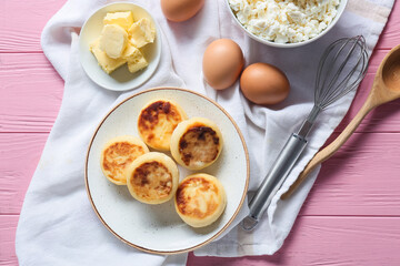 Plate with tasty cottage cheese pancakes and ingredients on pink wooden background