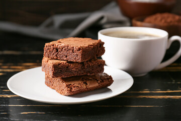 Plate with pieces of tasty chocolate brownie on black wooden background
