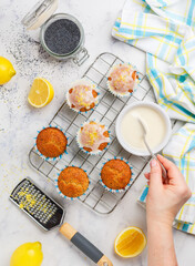 Women's hands decorate sugar icing on freshly baked cupcakes with poppy seeds and lemon zest on a marble background. The concept of home baking. Citrus dessert. Breakfast for gourmets