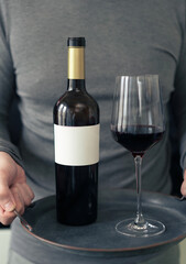 Man holding a tray with bottle and glass of red wine