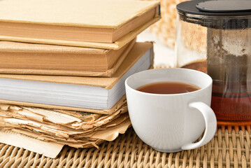 Stack of books with cup and teapot on wicker tray, closeup
