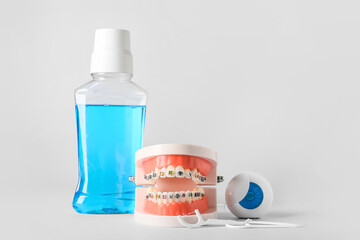 Model of jaw with braces, toothpicks, floss and mouthwash on white background