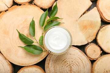 Jar with natural cosmetic cream and plant branch on wooden background