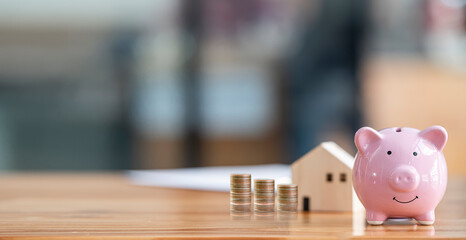 Piggy bank and house model on wooden table with copy space, panoramic background. Financial and...