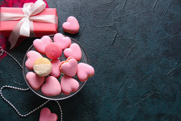 Dessert stand with tasty heart-shaped macaroons and gift box on black background