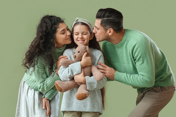 Happy parents kissing their little daughter on green background