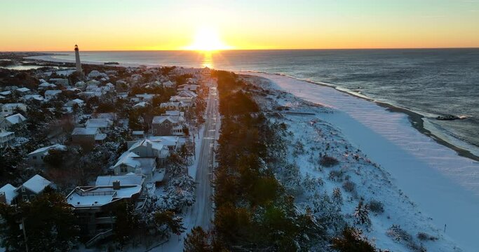 Homes In Seaside Beachfront Town. Lighthouse At Sunrise. Snow-covered Sand Dunes. Aerial Truck Shot.