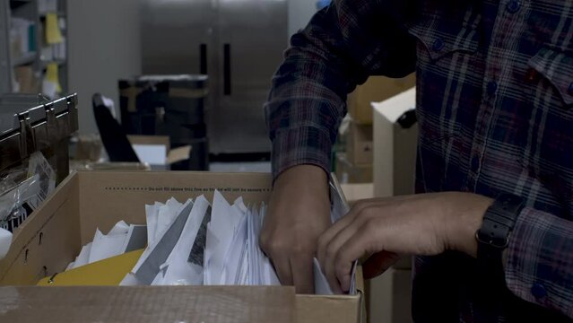 A close up shot of the hands of an Indian man digging through a box of archived documents in a storeroom, the man searching for the original hard copy piece of paper