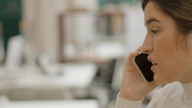 Face Close-up Of Beautiful Businesswoman Talking On Phone During Working Day Indoors, Busy Lady Making An Important Call, Sitting In A Bright Modern Office - Side View