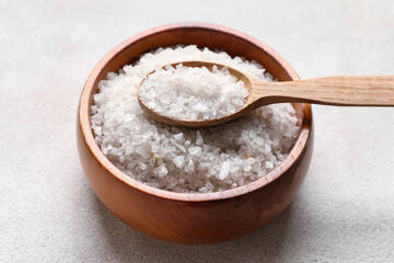 Wooden bowl with sea salt and spoon on light background, closeup