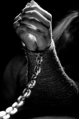Women's hands are tied with a rope and shackled with a metal chain