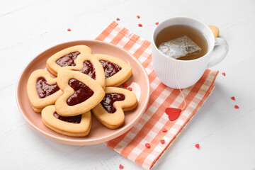 Plate with tasty cookies and cup of tea for Valentine's Day celebration on light background