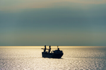 silhouettes of ship at sea, dramatic seascape with sunset sky, bright sunlight reflected from the waves
