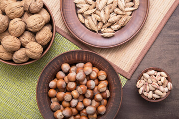 Various nuts mix in brown clay plates. Walnut, hazelnut, almond, pistachio and nutcracker on rustic background, top view, flat lay